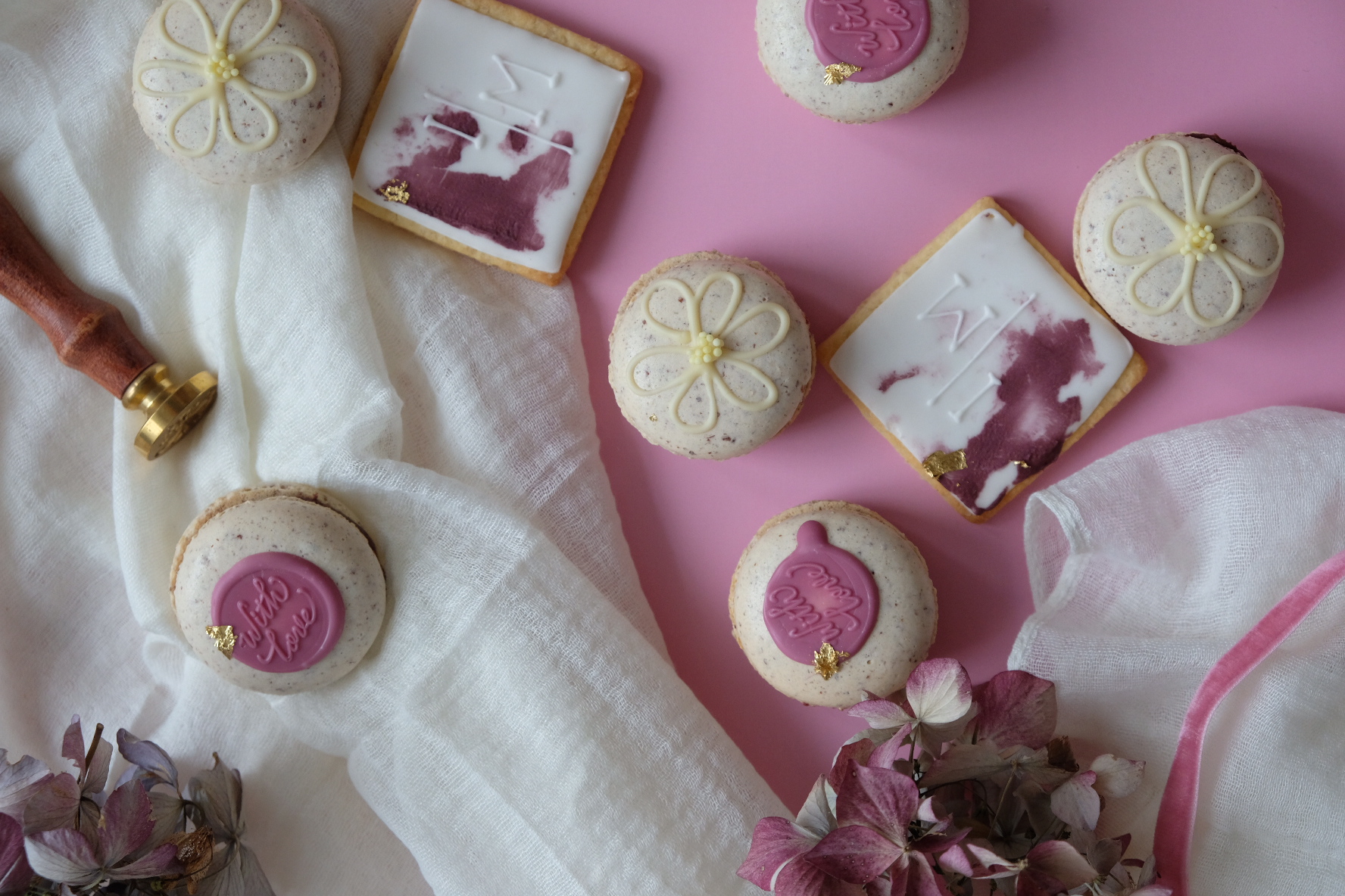 Feine handgemachte Pralinen in den Farben weiß und rosa mit Stempeldruck "With love" sowie Blümchen liegen auf einem weißen Tuch mit rosa Hintergrund.