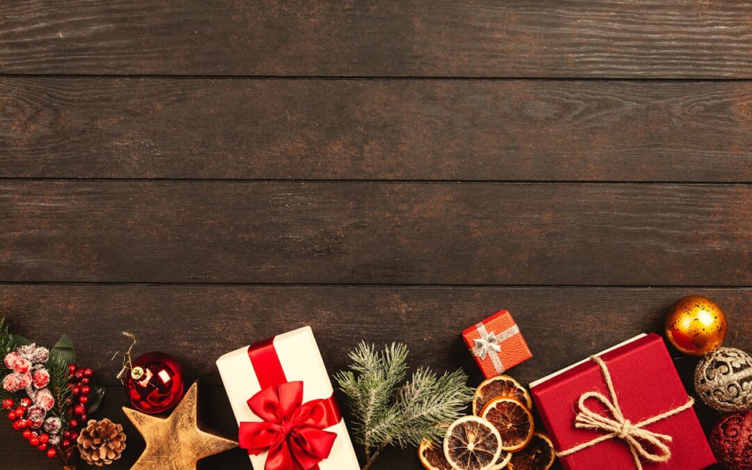 Dunkler Holzhintergund, am unteren Rand verpackte Gescehnke, Sterne, Tannenzweige und getrocknete Orangenscheiben